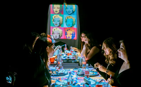 Guests dining at a table with pop art projections during the Seven Paintings Immersive Dining Show.