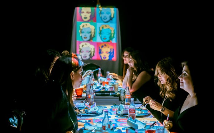 Guests dining at a table with pop art projections during the Seven Paintings Immersive Dining Show.