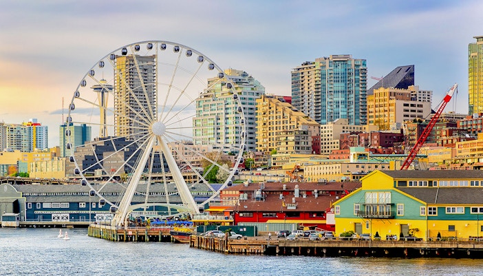 Seattle waterfront with The Wheel at ICON Park and skyline at dusk.