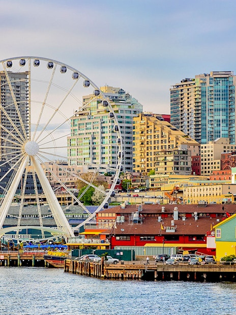 Seattle waterfront with The Wheel at ICON Park and skyline at dusk.