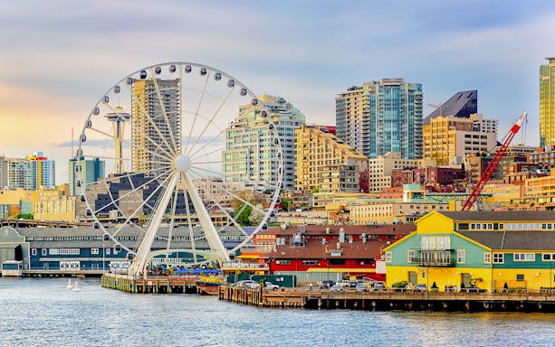 Seattle waterfront with The Wheel at ICON Park and skyline at dusk.