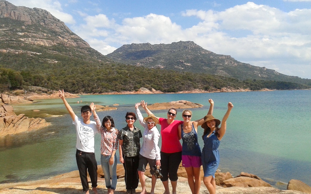 Group of tourists enjoying the view at Wineglass Bay, Tasmania, with mountains and clear water in the background.