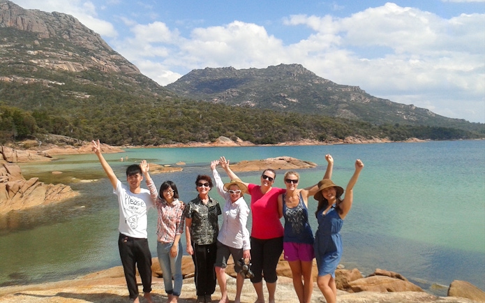 Group of tourists enjoying the view at Wineglass Bay, Tasmania, with mountains and clear water in the background.