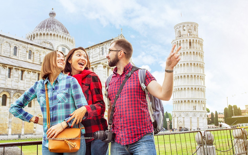 Tourists enjoying a guided tour at the Baptistery and Cathedral with the Leaning Tower of Pisa in the background.