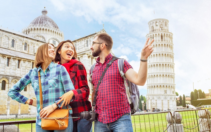 Tourists enjoying a guided tour at the Baptistery and Cathedral with the Leaning Tower of Pisa in the background.