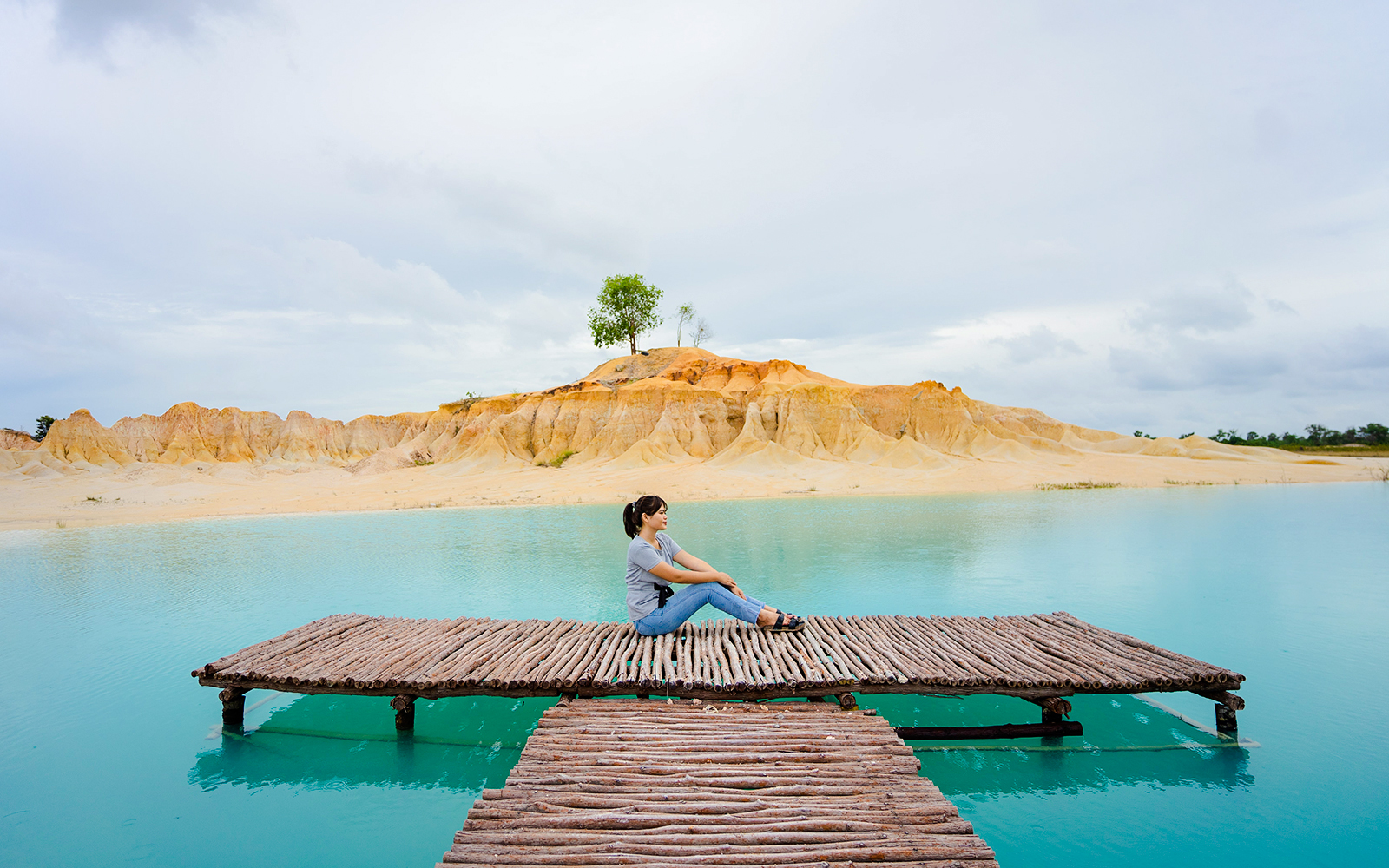 Woman sitting on pier at Blue Lake, Bintan Mini Desert in the background.