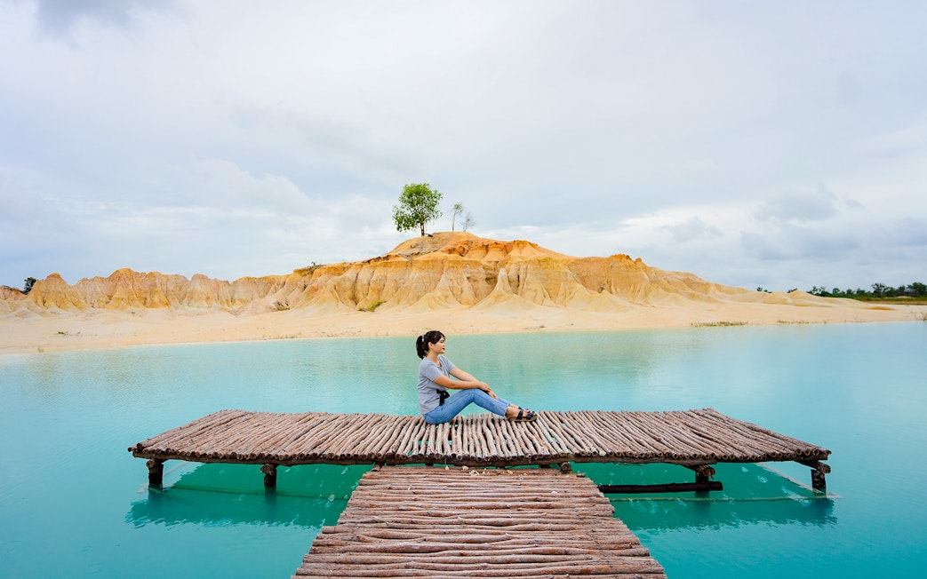Woman sitting on pier at Blue Lake, Bintan Mini Desert in the background.