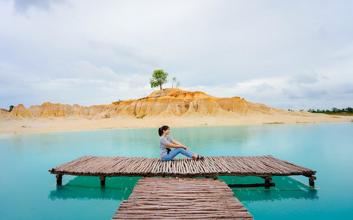 Woman sitting on pier at Blue Lake, Bintan Mini Desert in the background.