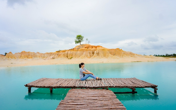Woman sitting on pier at Blue Lake, Bintan Mini Desert in the background.