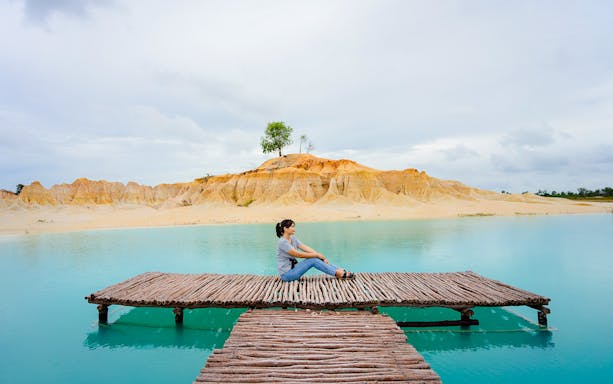 Woman sitting on pier at Blue Lake, Bintan Mini Desert in the background.