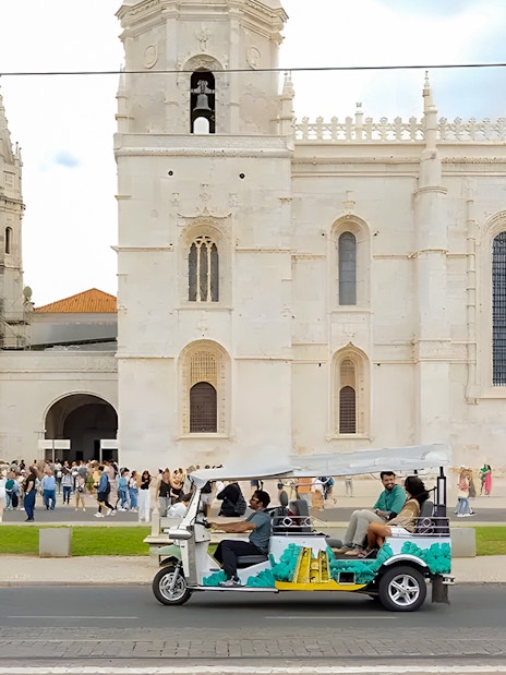 Tourist on eco tuk-tuk passing Jeronimos Monastery in Lisbon.