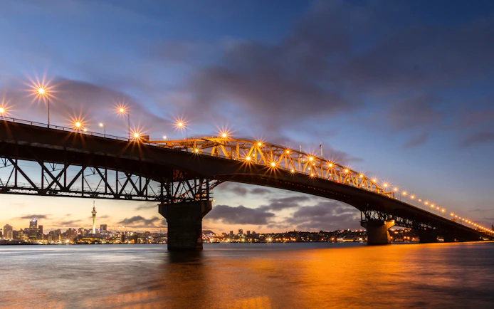 Auckland Harbour Bridge illuminated at dusk with city skyline in the background.