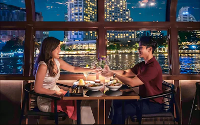 Couple dining on Saffron Luxury Cruise by Banyan Tree with cityscape view.