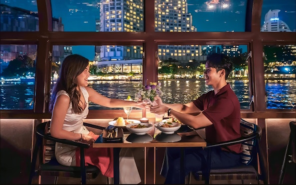Couple dining on Saffron Luxury Cruise by Banyan Tree with cityscape view.
