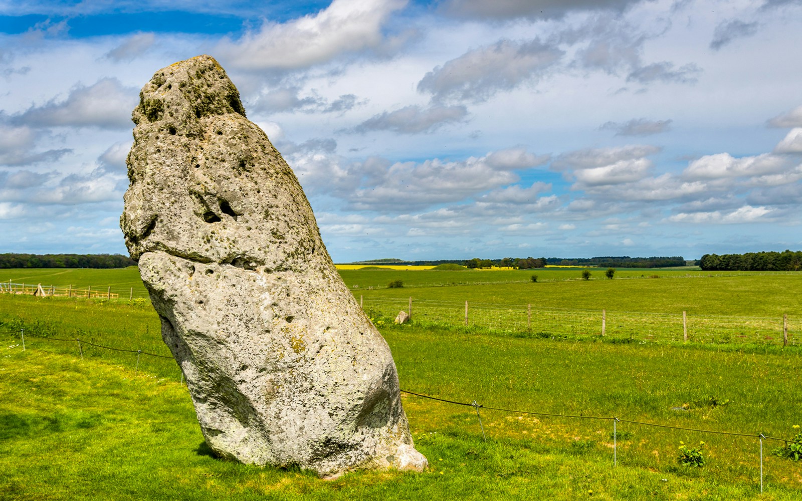 Heel Stone at Stonehenge with green fields and blue sky in the background.