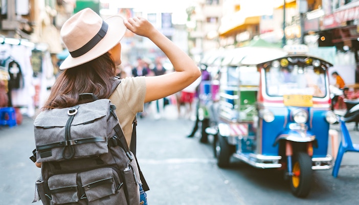 Tourist walking through vibrant Bangkok street market.