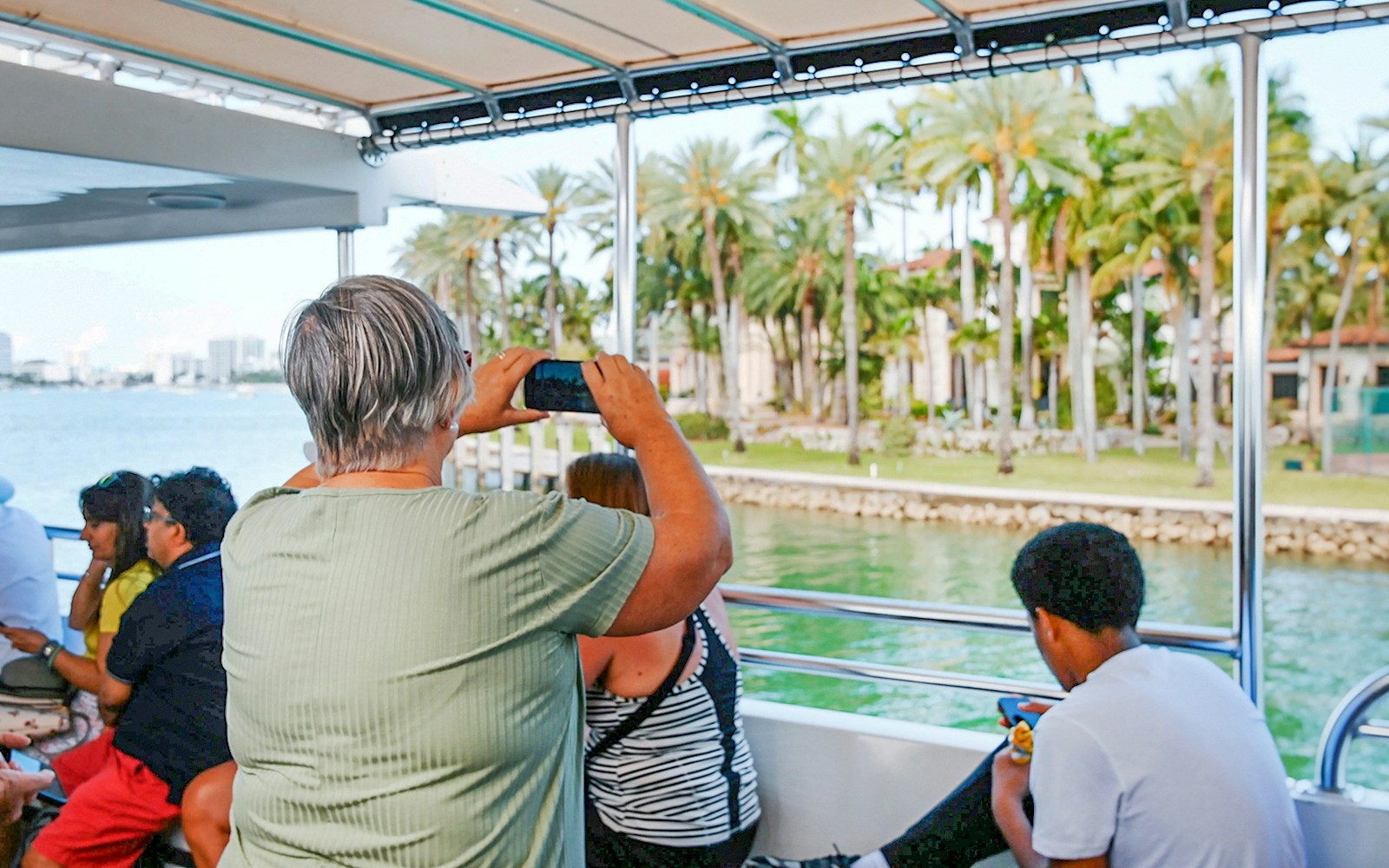 Guests capturing photos of celebrity homes from a boat on Biscayne Bay during a sightseeing cruise in Miami.