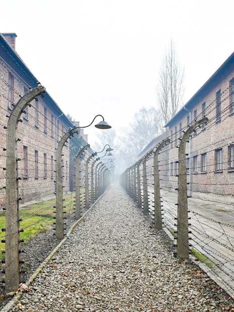 Auschwitz I barracks with barbed wire fences along a gravel path.