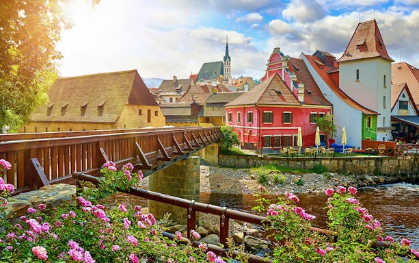 Cesky Krumlov street view with colorful buildings and a wooden bridge over a river.