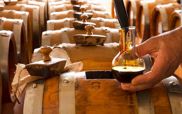 Vinegar being poured from a glass flask into a wooden barrel during a guided cellar tour.