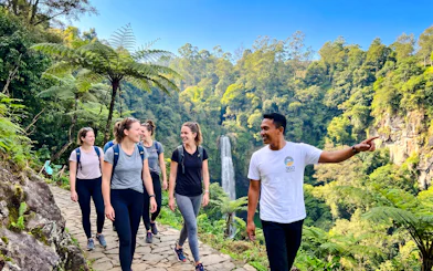 Group hiking near Curug Cimahi waterfall, Bandung, with guide pointing out sights.