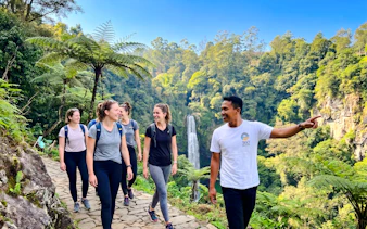 Group hiking near Curug Cimahi waterfall, Bandung, with guide pointing out sights.