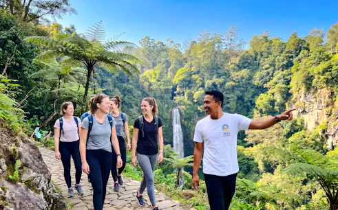 Group hiking near Curug Cimahi waterfall, Bandung, with guide pointing out sights.