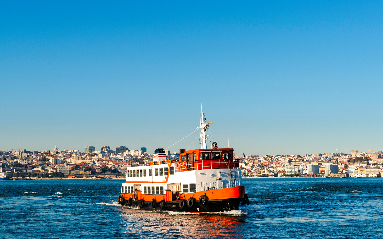 Cacilheiro ferry crossing the Tagus River with Lisbon skyline in the background.