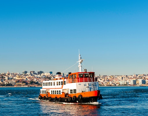Cacilheiro ferry crossing the Tagus River with Lisbon skyline in the background.