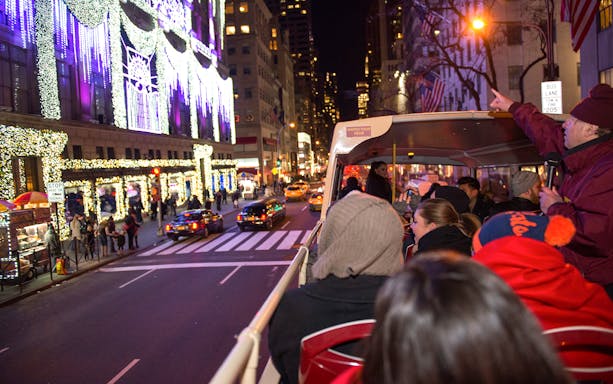 Open-top bus tour viewing holiday lights on New York City street.