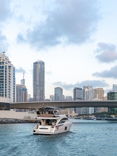 Luxury yacht cruising through Dubai Marina with city skyline in the background.