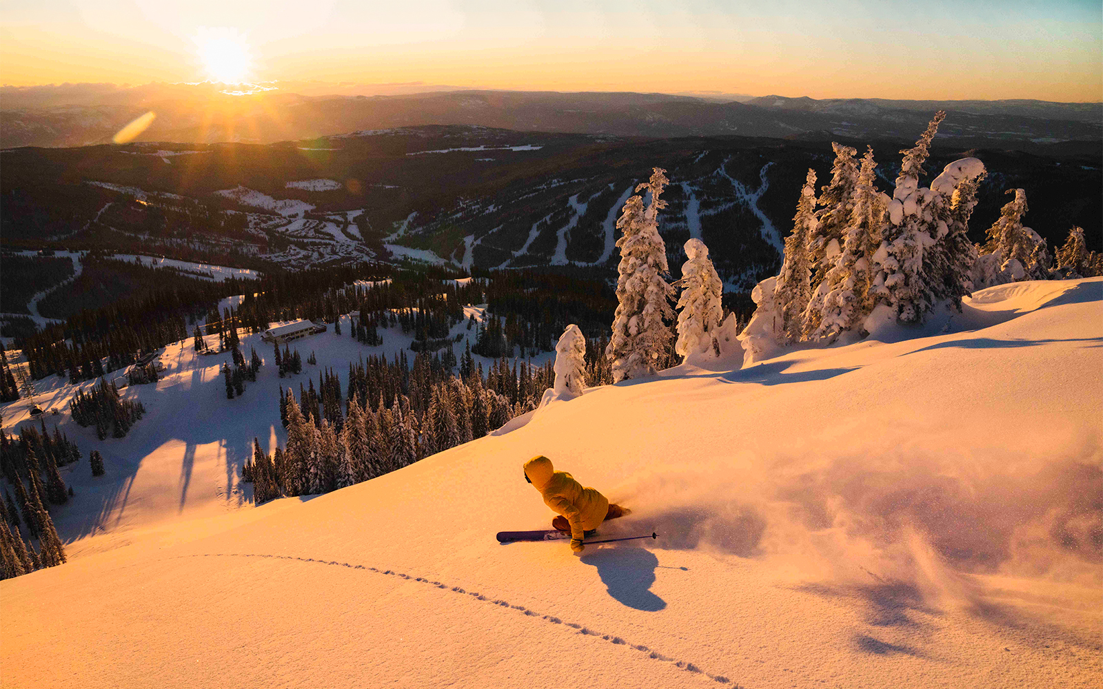 Skier descending a snowy slope at sunset, showcasing a scenic view of a ski resort with the Ikon Pass.