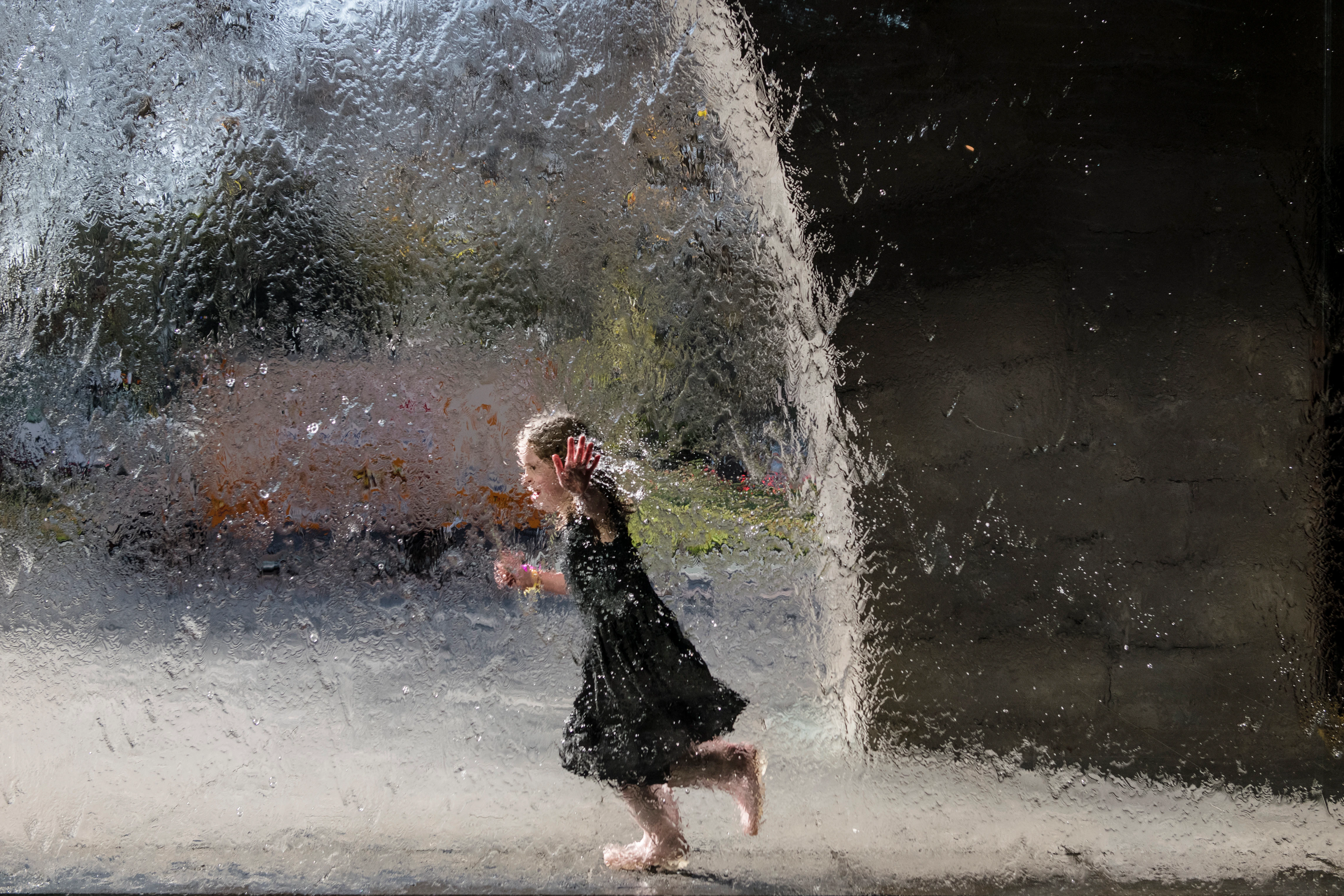 Young visitor running behind the waterwall at NGV International.