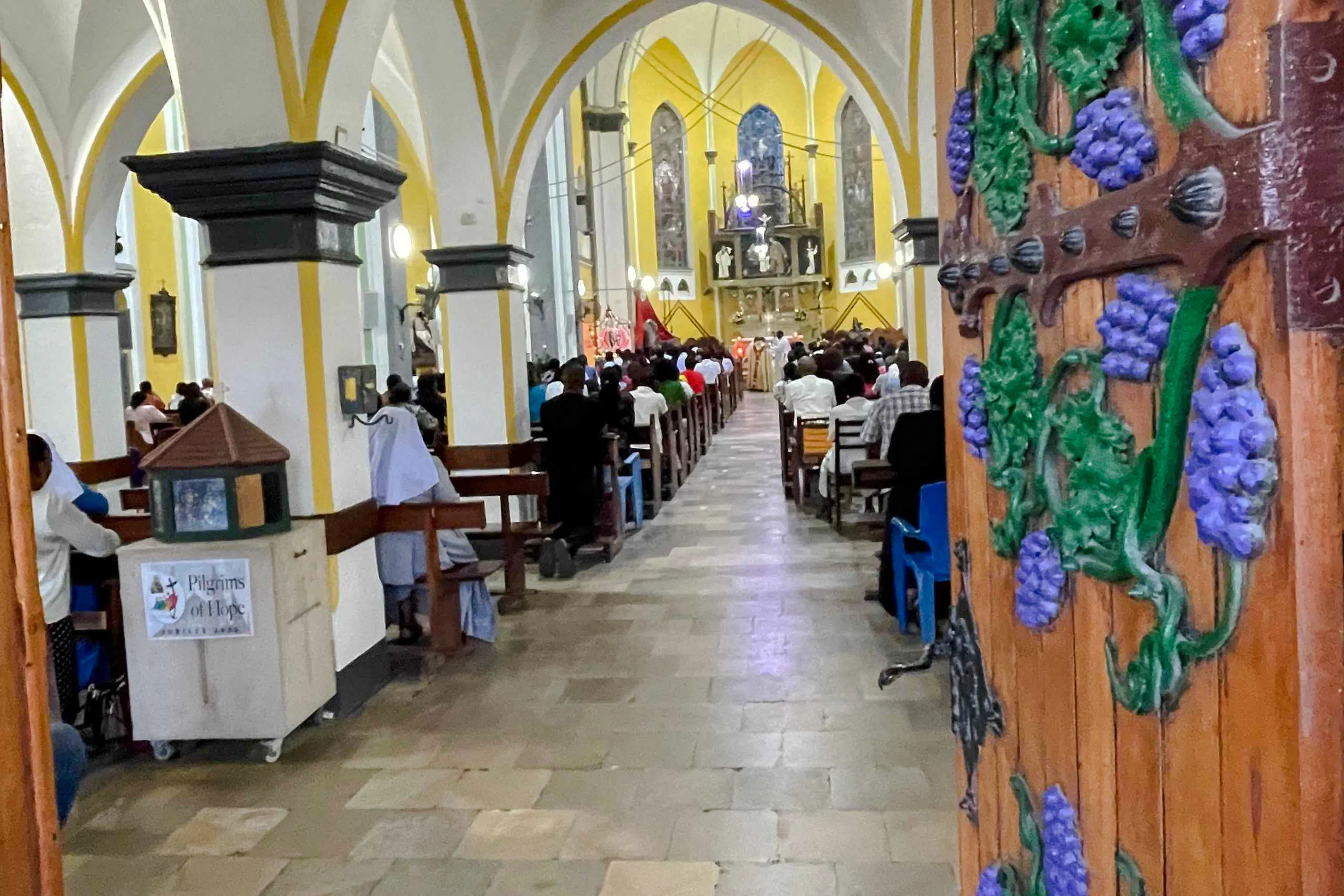 Interior of a church in Zanzibar with people attending a service, visible ornate wooden door.