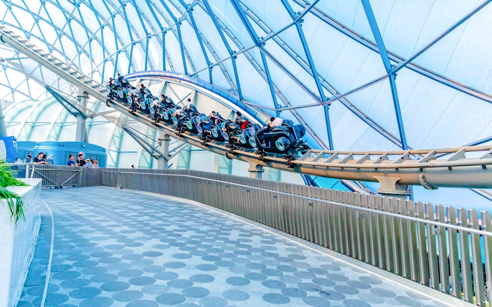 Visitors riding TRON Lightcycle Power Run roller coaster in futuristic setting.