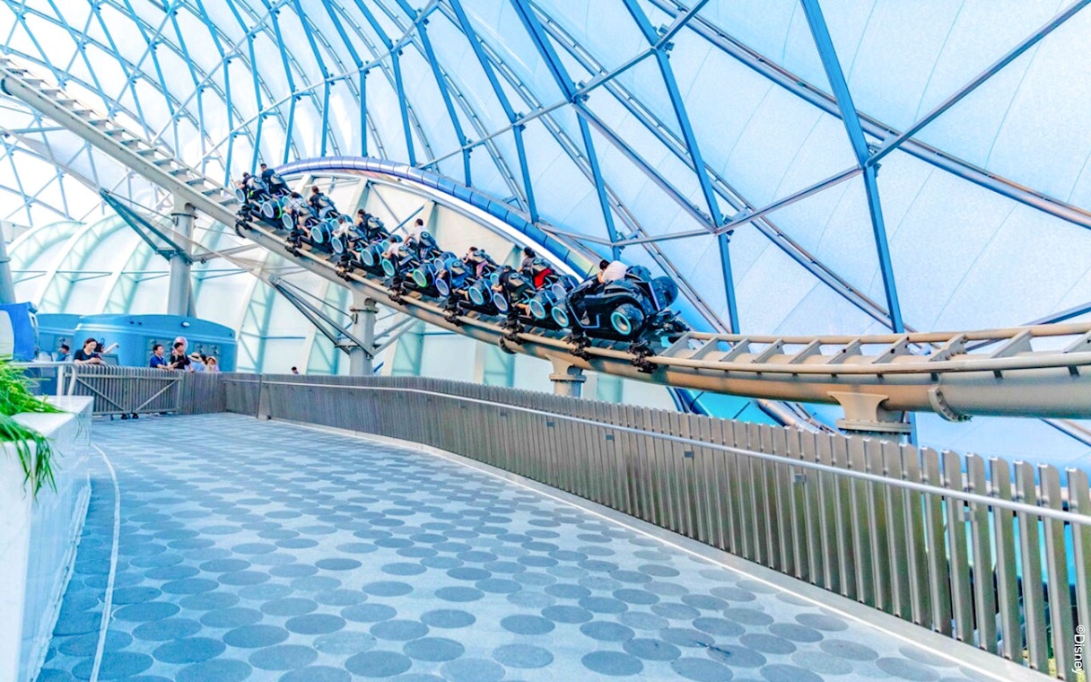 Visitors riding TRON Lightcycle Power Run roller coaster in futuristic setting.
