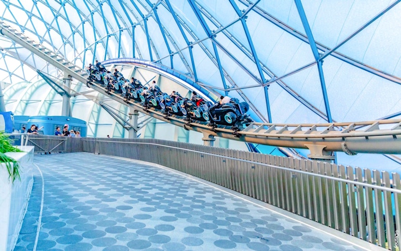 Visitors riding TRON Lightcycle Power Run roller coaster in futuristic setting.