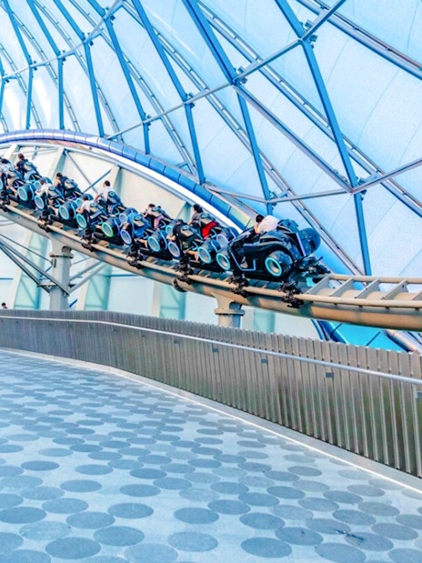 Visitors riding TRON Lightcycle Power Run roller coaster in futuristic setting.