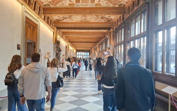 Visitors walking through a sculpture-lined corridor in Florence's Accademia Gallery.