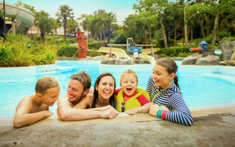 Family enjoying the pool at Alton Towers Waterpark with slides and greenery in the background.