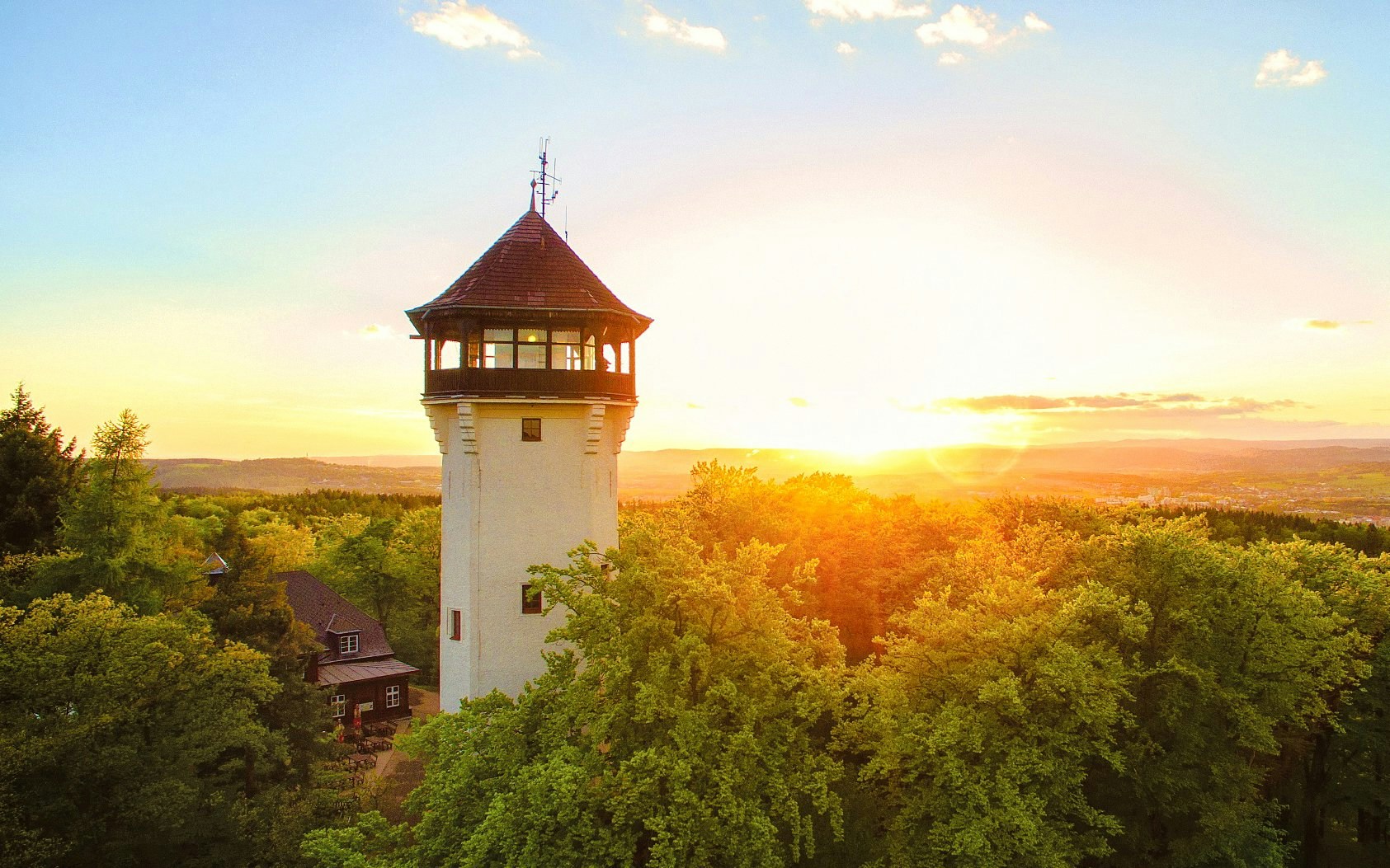 Diana Tower in Karlovy Vary surrounded by lush trees at sunset.