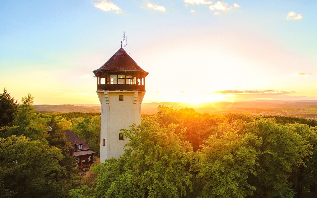 Diana Tower in Karlovy Vary surrounded by lush trees at sunset.