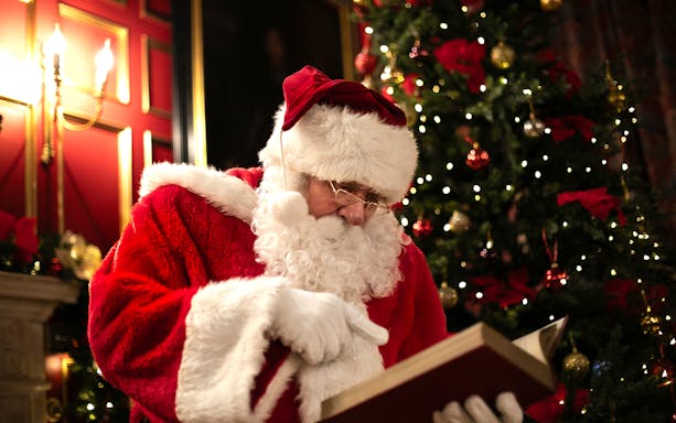Santa reading a book by a decorated Christmas tree at Warwick Castle.
