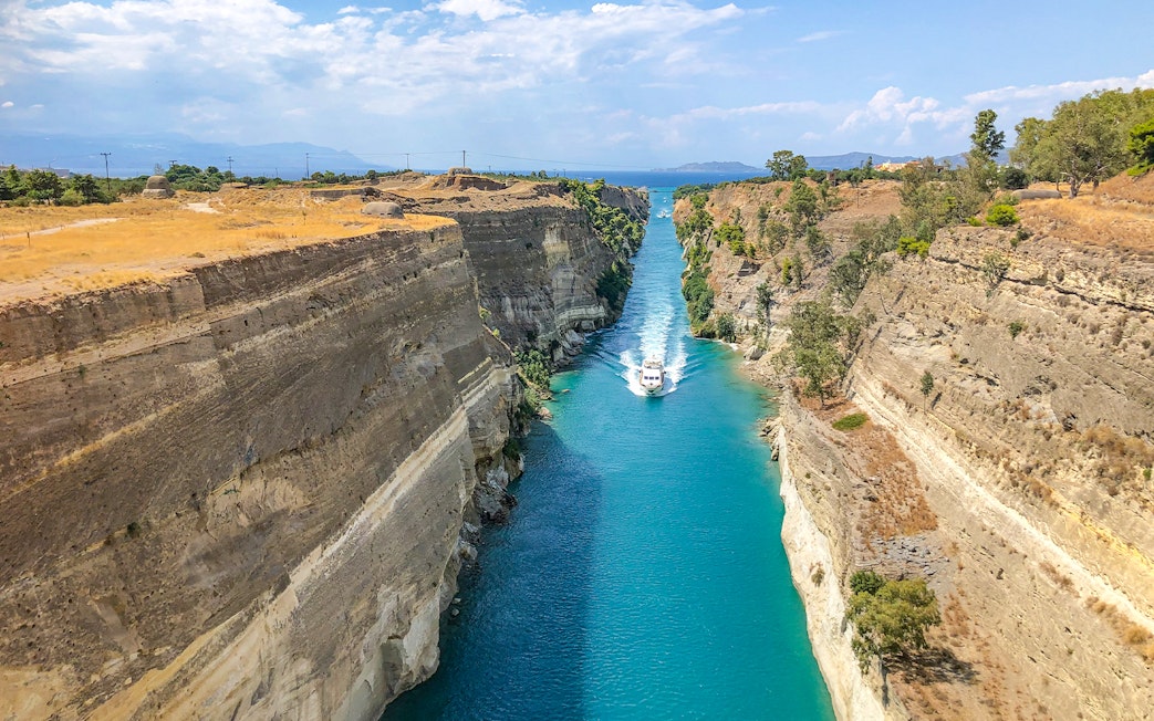 Boat navigating through the Corinth Canal, Greece, with steep rock walls and clear blue water.