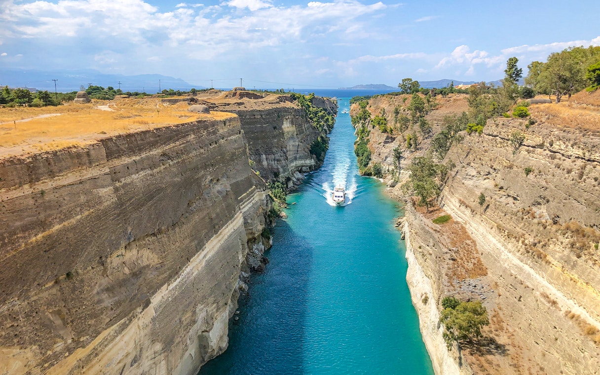 Boat navigating through the Corinth Canal, Greece, with steep rock walls and clear blue water.