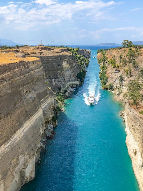 Boat navigating through the Corinth Canal, Greece, with steep rock walls and clear blue water.
