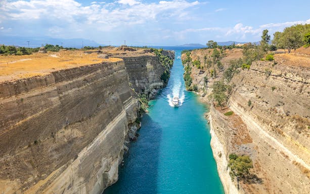 Boat navigating through the Corinth Canal, Greece, with steep rock walls and clear blue water.