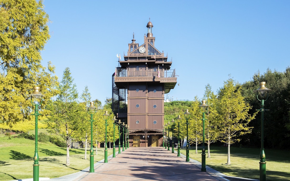 Ghibli Park tower with green lampposts and trees lining the pathway.
