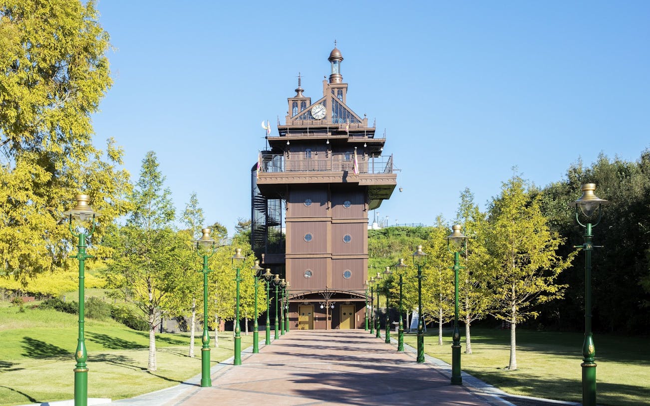Ghibli Park tower with green lampposts and trees lining the pathway.