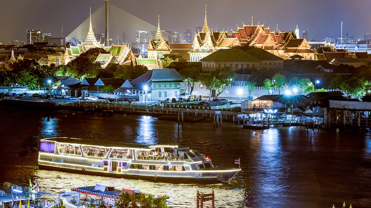 Cruise ship on Chao Phraya river with the Grand Palace in the background at night